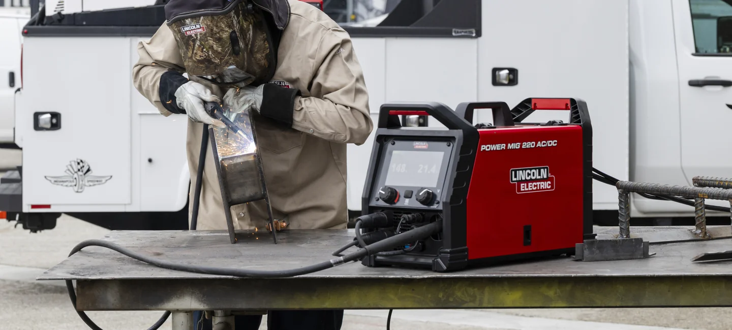 Welder using Lincoln Electric POWER MIG 220 AC/DC equipment beside a service truck